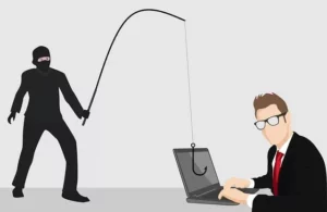 A person dressed in black looking like a ninja is holding a fishing pole in front of a man's laptop with the hook in front of the monitor. This is a representation of the cybersecurity term phishing